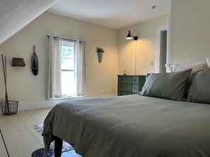 Una camera da letto con un letto, una cassettiera, una lampada, una finestra con tende e una pianta.