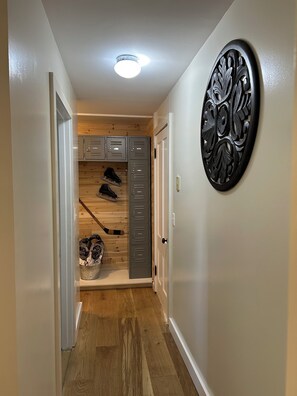 Un corridoio con pavimento in legno, una luce a soffitto, un appendiabiti con vari oggetti e un elemento decorativo al muro.
