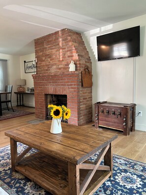 Un soggiorno con camino in mattoni, un tavolino in legno, una TV a parete e un tappeto decorato.