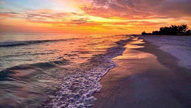 Een strand met golven, een zonsondergang en een heldere lucht.