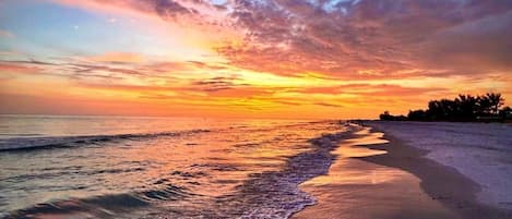 A beach with waves, a sunset, and a clear sky.