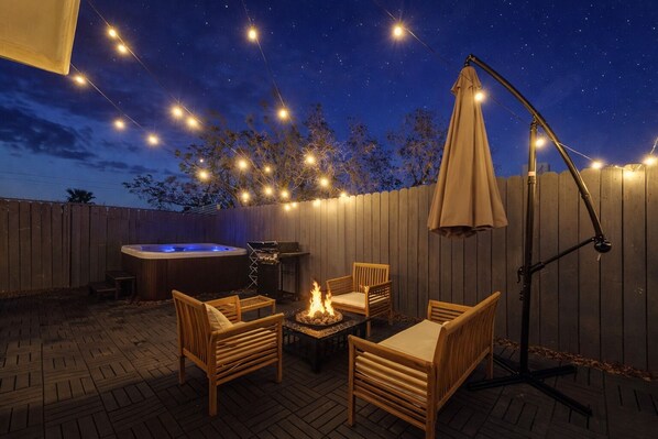 An outdoor patio with a hot tub, barbecue, and seating area under string lights. - Joshua Tree Oasis - 10 Min to Park - Hot Tub, Fire Pit & Stargazing (Joshua Tree)