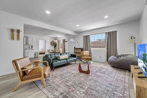 A modern living room with a green sofa, leather chairs, a coffee table, and a dining area with a table and chairs. - Joshua Tree Oasis - 10 Min to Park - Hot Tub, Fire Pit & Stargazing (Joshua Tree)