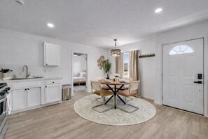 A compact kitchen with white cabinets, a dining area with a round table, and a separate sleeping area. - Joshua Tree Oasis - 10 Min to Park - Hot Tub, Fire Pit & Stargazing (Joshua Tree)