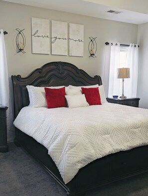 Ein Bett mit dunklem Kopfteil, weißer Bettwäsche und roten Kissen. Darüber an der Wand hängen drei gerahmte Kunstwerke.