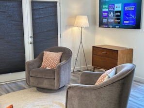 A living room with a sofa, a chair, a lamp, and a TV displaying a streaming service interface.