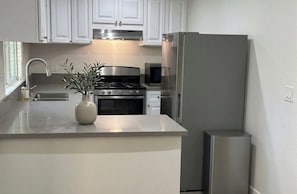 A modern kitchen with white cabinets, stainless steel appliances, and a marble countertop.