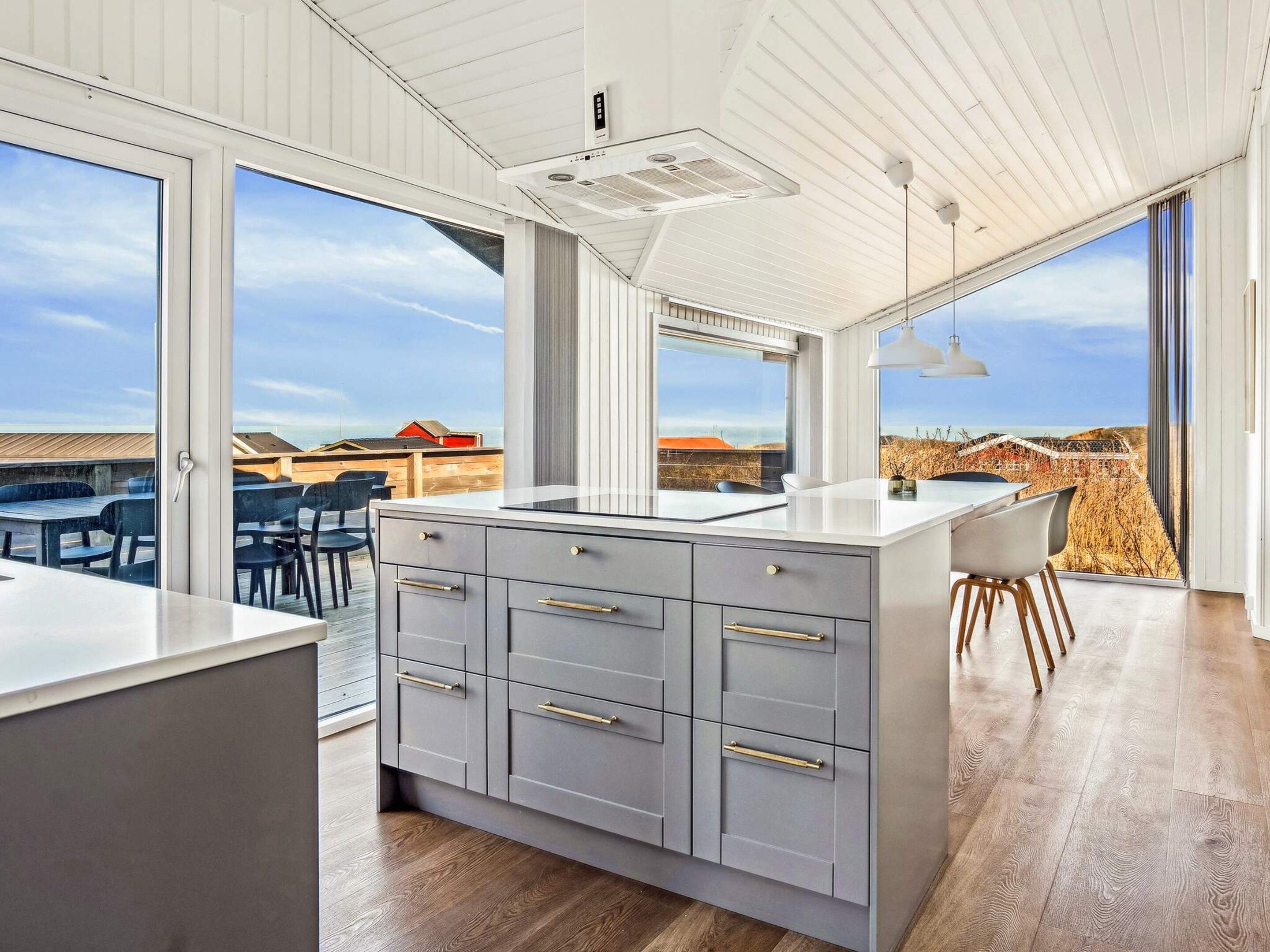 A modern kitchen with a large island, sliding doors to a balcony, and a view of the landscape.