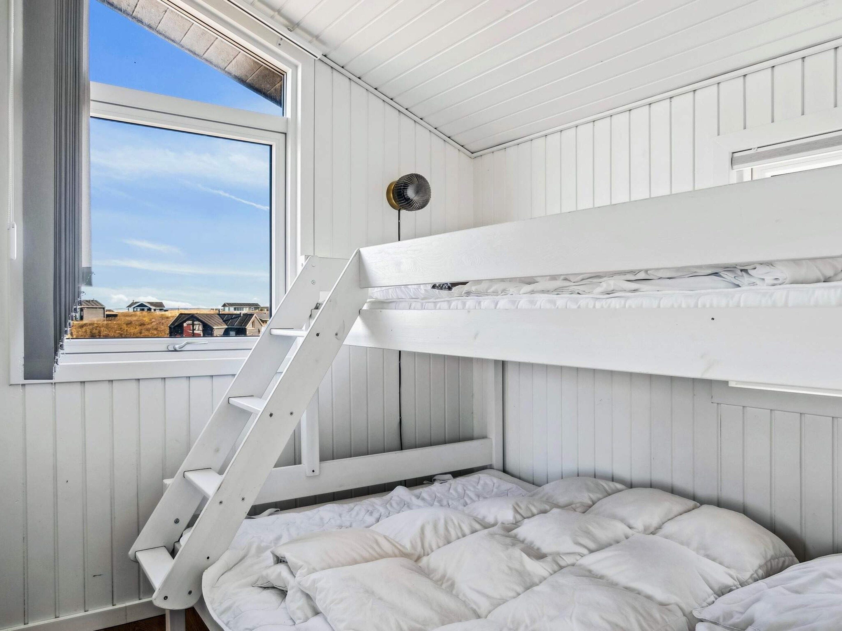 Une chambre avec un lit superposé, une échelle, une fenêtre et une vue sur un paysage rural.