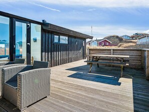 Una terraza de madera con mobiliario de mimbre y una mesa de picnic.