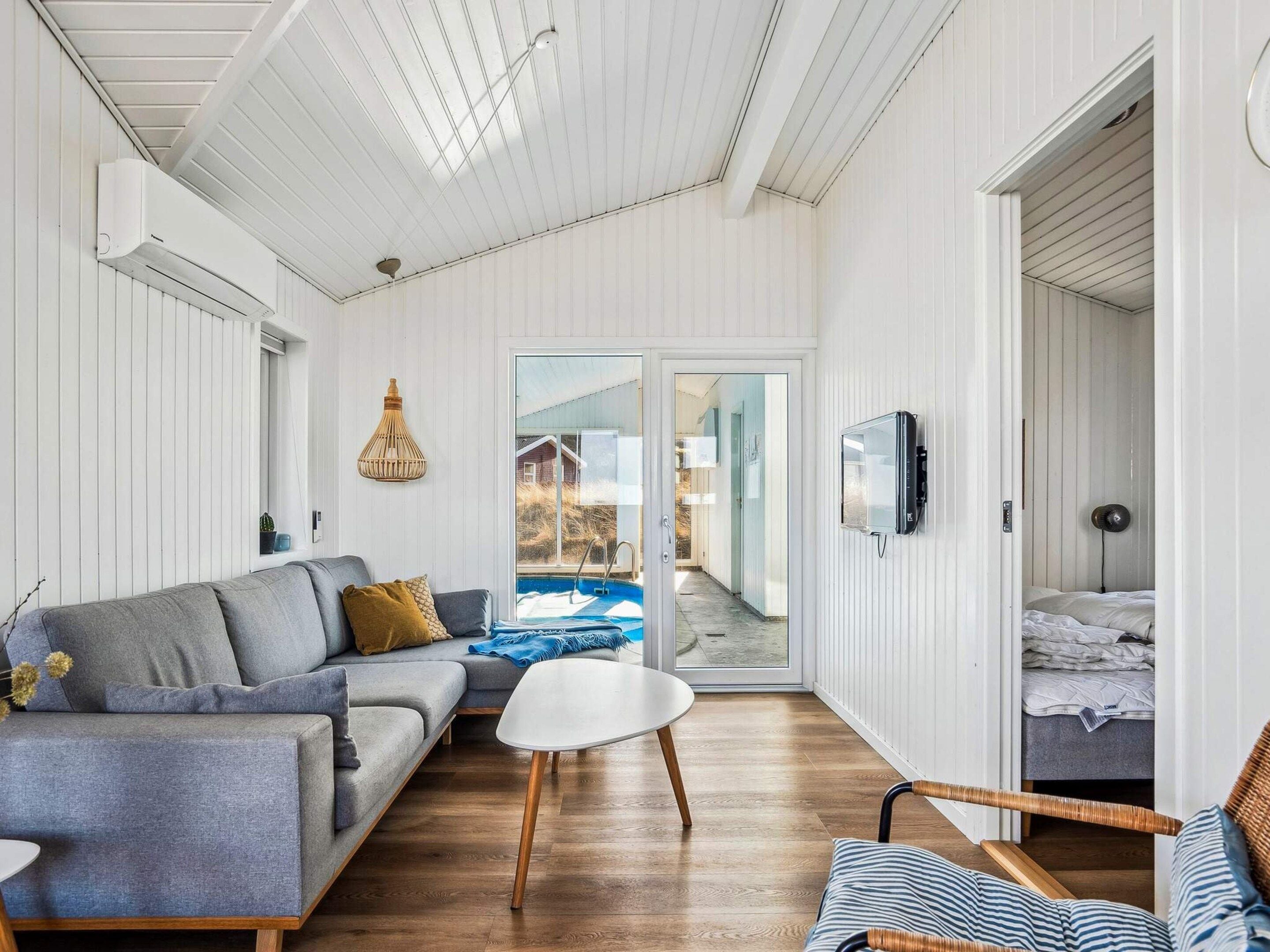 A modern living room with a sofa, a small table, and a view of a pool through glass doors.