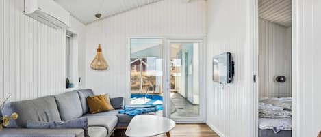 A modern living room with a sofa, a small table, and a view of a pool through glass doors.