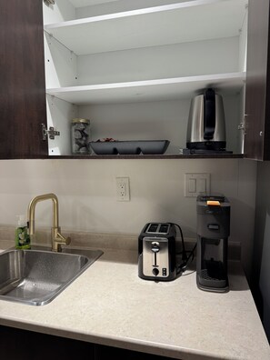 A kitchen with a sink, a toaster, a coffee maker, and a shelf above the counter. - Brand-New Cozy Luxury Suite |Private Entrance (Brampton)