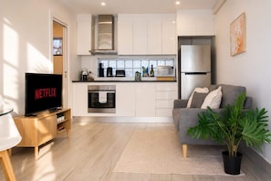 A modern kitchen with integrated appliances, a grey sofa, and a television displaying 'NETFLIX'. - The Den | Charming 1BR Glebe, Near Sydney Uni (Glebe)