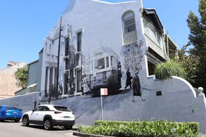 A building with a mural of historical figures and a tram, parked cars, and a clear sky. - The Den | Charming 1BR Glebe, Near Sydney Uni (Glebe)