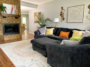 A living room with a fireplace, a sectional sofa, a patterned rug, and decorative wall art.