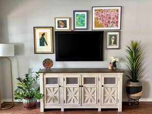A living room with a TV mounted on the wall, a cabinet with glass doors, and various framed artworks.