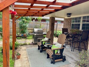 A covered patio with a grill, outdoor seating, and a wooden pergola.