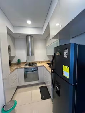 Eine kleine Küche mit Einbauofen, Edelstahl-Dunstabzugshaube und einem schwarzen Kühlschrank.