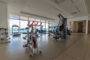 Ein geräumiger Fitnessraum mit unterschiedlichen Trainingsgeräten, großen Fenstern und Blick auf die Stadt.
