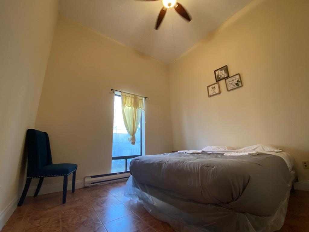 A bedroom with a bed, a chair, a ceiling fan, and a window with curtains.
