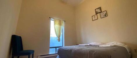 A bedroom with a bed, a chair, a ceiling fan, and a window with curtains.