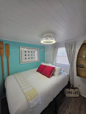 A bedroom with a bed, a wall-mounted light fixture, a window with curtains, and a wall-mounted shelf.