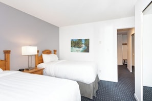 A hotel room with two beds, a nightstand with a lamp, a painting of a waterfall, and a carpeted floor. - Whistler Creekside Ski in/Ski out Condo with Pool (Whistler)