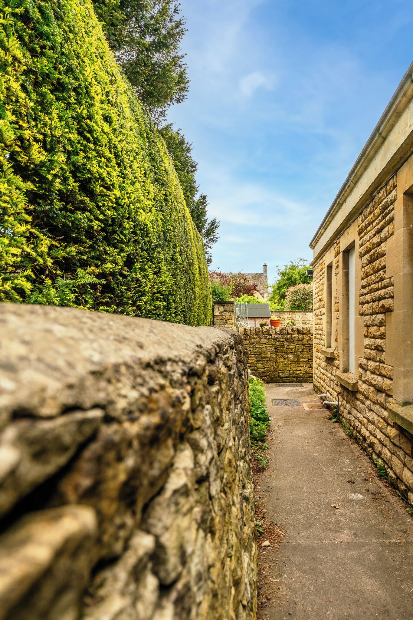 A stone wall, a narrow pathway, and a building with windows.