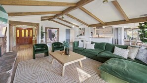 Un salon spacieux avec un haut plafond, des poutres apparentes, un canapé vert et un coin repas.