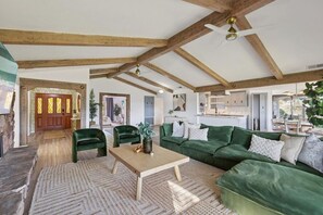 Uma sala de estar espaçosa com teto alto, vigas de madeira, um conjunto de sofá verde e uma área de jantar.