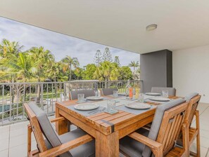 Ein Holzespeisesaal, gedeckt für vier Personen, mit Stühlen, einem Balkon mit Geländer und Blick auf Palmen und Grünpflanzen.