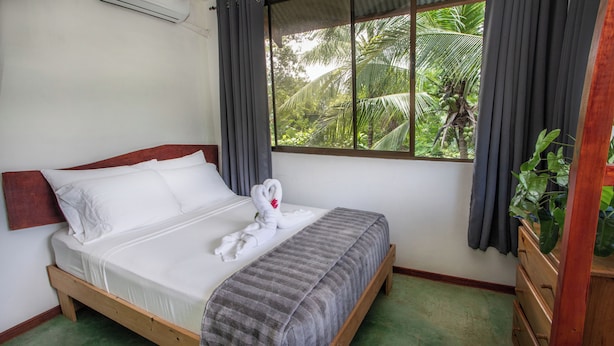A bed with white linens, a grey striped blanket, and a towel with a red flower. - 2-bedroom A/C Apartment in Quepos (Quepos)