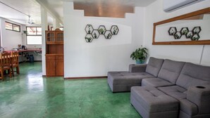 A living room with a sectional sofa, a dining area with chairs, a kitchen with cabinets, and hexagonal wall art. - 2-bedroom A/C Apartment in Quepos (Quepos)