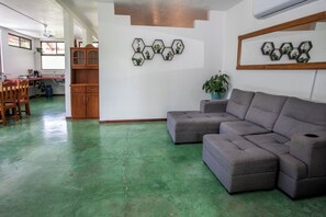 A living room with a sectional sofa, a dining area with chairs, a kitchen with cabinets, and hexagonal wall art. - 2-bedroom A/C Apartment in Quepos (Quepos)