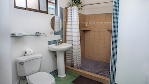 A bathroom with a toilet, sink, shower, and a small shelf with toiletries. - 2-bedroom A/C Apartment in Quepos (Quepos)