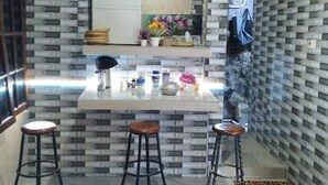 A kitchen with a white countertop, three stools, a refrigerator, and a decorative mirror. - Cozzy Ida Guest House (Sukawati)