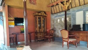 A room with a wooden cabinet, two chairs, a desk, and a television. - Cozzy Ida Guest House (Sukawati)