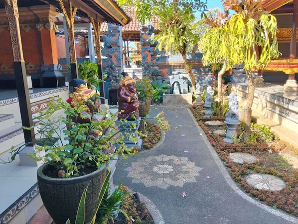 A pathway lined with statues and potted plants, leading to a traditional building with ornate architecture.