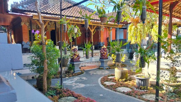 A courtyard with a tiled roof, potted plants, and statues. - Cozzy Ida Guest House (Sukawati)