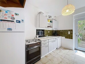 Eine Küche mit Gasherd, Backofen, Mikrowelle und Spüle. An der Wand hängt ein Kalender und eine Pendelleuchte.