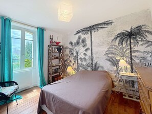 A bedroom with a bed, a window with curtains, a wall tapestry, a shelf with items, and a lamp. - QUIBERON - 4 room villa - 90m2 - City center (QUIBERON)