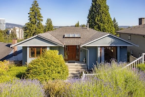 A two-story house with a front porch, a chimney, and a view of the city in the background. - Cozy 3BD Retreat, North Van Balcony Views (North Vancouver)