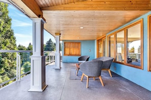 A covered balcony with a view of trees, a wooden ceiling, and wicker chairs. - Cozy 3BD Retreat, North Van Balcony Views (North Vancouver)