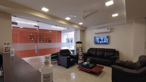 A modern lobby with a reception desk, leather sofas, a coffee table, and a television mounted on the wall. - Corporate Stays (Chengalpattu)