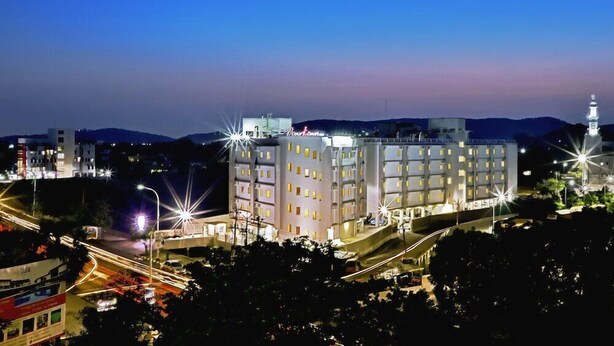 A multi-story hotel with a central courtyard, surrounded by trees and a road with traffic lights. - Corporate Stays (Chengalpattu)