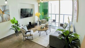 A modern living room with a flat-screen TV, comfortable seating, a coffee table, and large windows offering a view. - Modern Ocean View Apartment in Av. Balboa King Bed, Pool & Gym (Panamá)