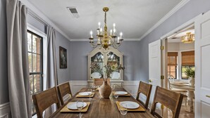 Ein Esszimmer mit einem Holztisch, gedeckt für sechs Personen, einer Kristallleuchtre und einem großen Spiegel über dem Tisch.
