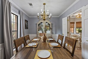A dining room with a wooden table set for six, a chandelier, and a large mirror above the table. - 5BR Near Graceland Sleeps 10 with Piano, Fire Pit, and Games (Memphis)
