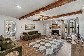 A spacious living room with a fireplace, wooden beams, and a large rug. - 5BR Near Graceland Sleeps 10 with Piano, Fire Pit, and Games (Memphis)